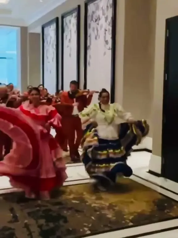 Dos bailarinas de ColombiArte con polleras rosada y de rayas girando en el salón de una boda, con mariachis detrás
