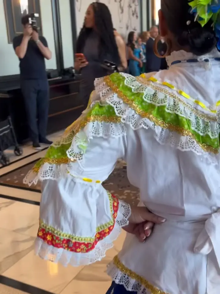 Bailarina de espaldas con traje blanco, cintas verdes y flores en el pelo, bailando en un salón de boda