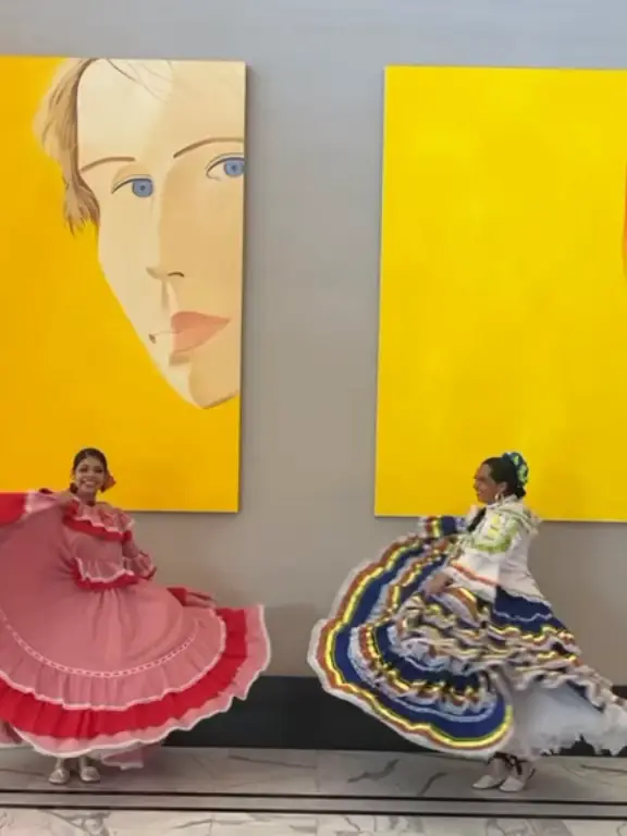 Dos bailarinas con polleras rosada y azul bailando frente a cuadros amarillos