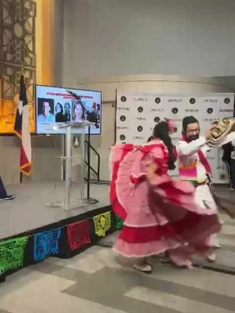 Bailarina con pollera rosada en pleno giro junto a su pareja con sombrero vueltiao, sobre una tarima con papel picado