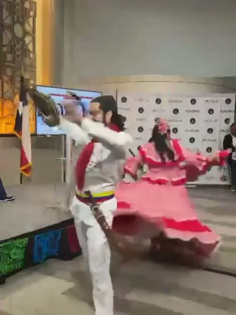 Bailarín de blanco levantando el sombrero vueltiao mientras la bailarina abre su pollera rosada en la tarima