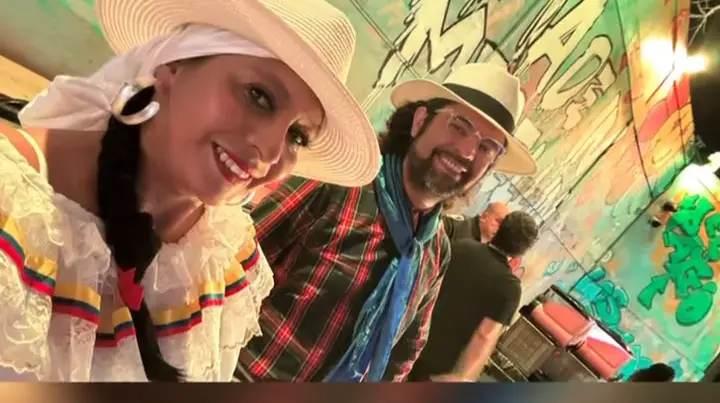 Pareja de ColombiArte con sombreros blancos sonriendo frente a un mural de colores