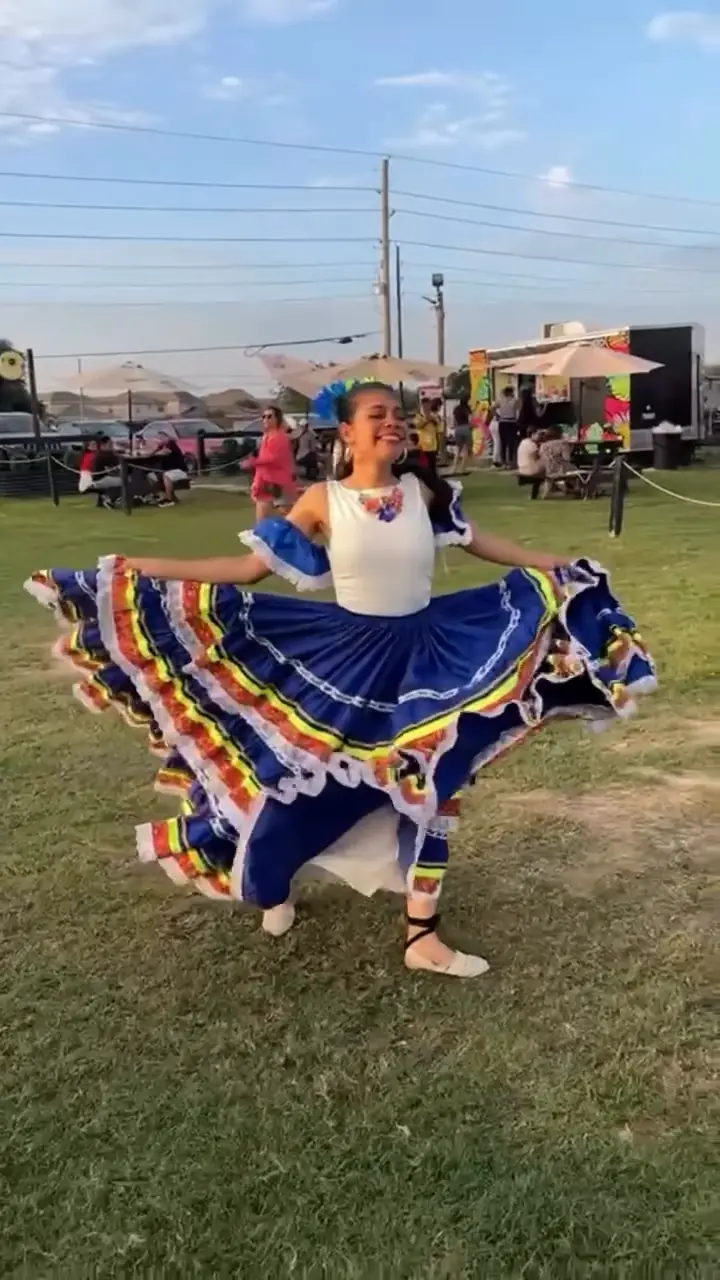 Bailarina de ColombiArte girando una pollera azul con cintas de colores sobre el césped de un festival al atardecer