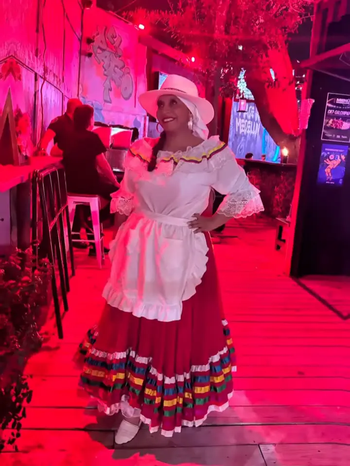 Bailarina con sombrero blanco, delantal y falda roja con cintas, bajo luces rojas